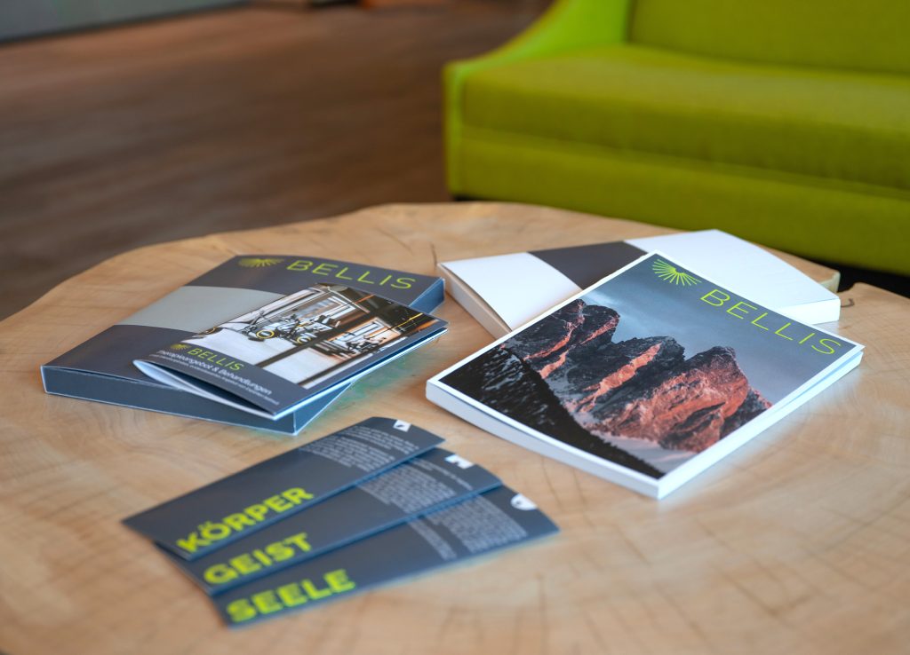 Broschüren, Magazin mit Bergmassiv und Karten Körper, Geist und Seele auf einem Holztisch für BELLIS