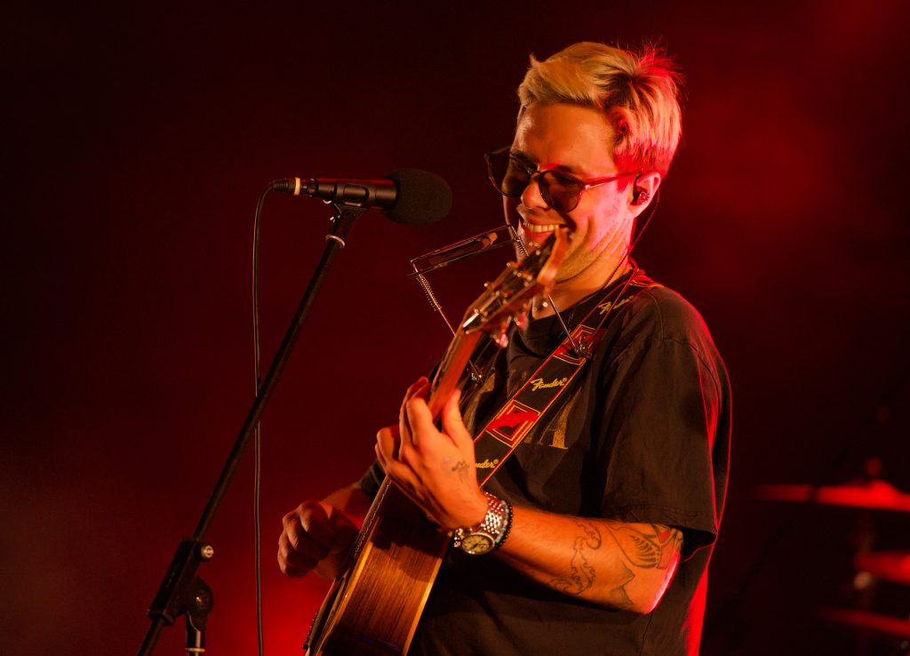 Sänger Oimara mit Sonnenbrille, Gitarre und Mundharmonika im roten Bühnenlicht, BK Open Air 2025, Fotografie von Artwerk Murnau