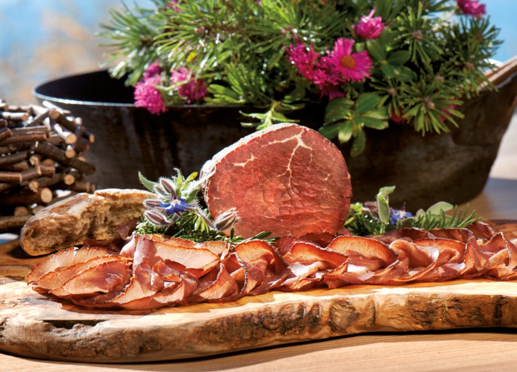 Aufgeschnittenes Fleisch auf Holzbrett mit Brot, Borretsch und rosa Astern im Hintergrund für kostbar