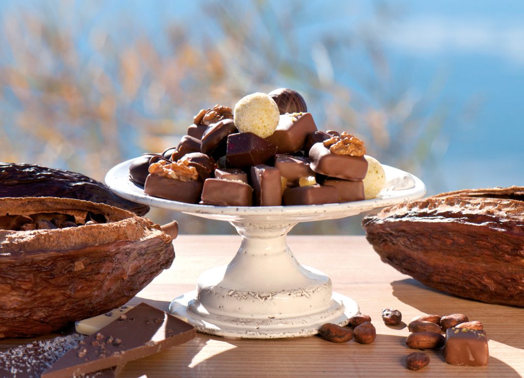 Pralinen mit Walnüssen und Schokoladentafeln auf weißer Etagere zwischen Kakaofrüchten und Kakaobohnen für kostbar